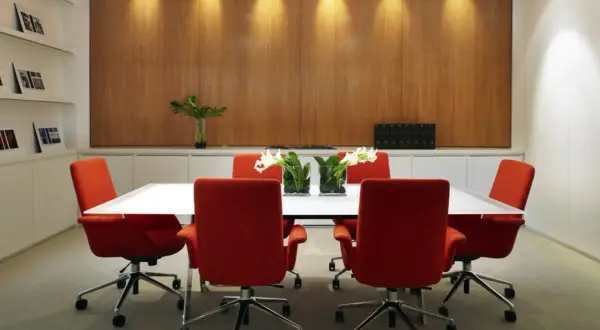Salle de réunion moderne avec chaises rouges vives et une table blanche épurée. La décoration salle de réunion est complétée par des vases de fleurs et un mur boisé chaleureux.