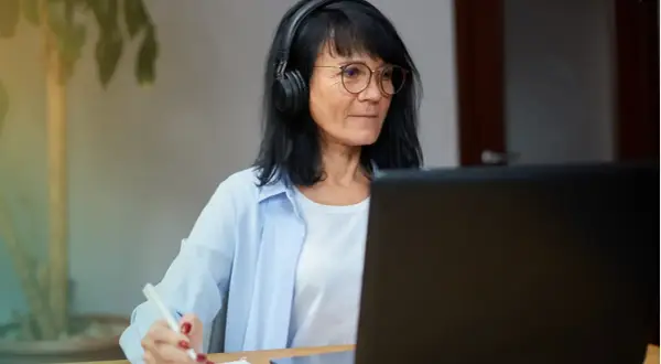 Femme avec casque et lunettes travaillant sur ordinateur portable, prenant des notes. Elle pratique le télétravail raison médicale.