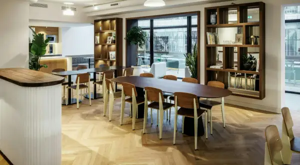 Aménagement locaux professionnels : espace lumineux avec tables, chaises en bois et étagères murales.