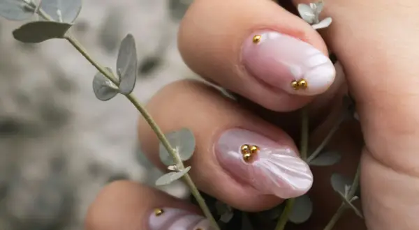 Manucure délicate aux perles dorées sur fond rose quartz, évoquant la douceur d'une fleur.