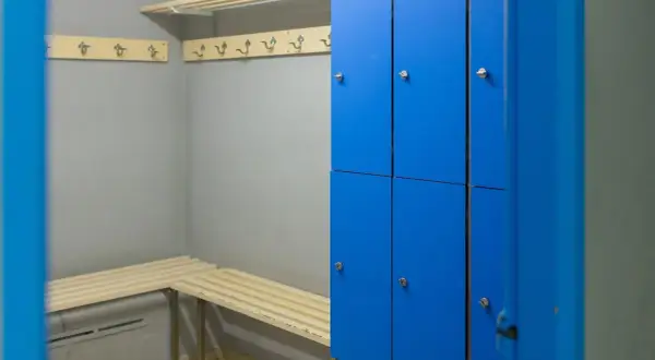 Vestiaire d'entreprise avec casiers personnels bleus, bancs en bois et patères.