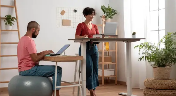 Un homme et une femme travaillent dans un bureau moderne. L'homme est assis sur un ballon de gym, la femme est en posture debout.