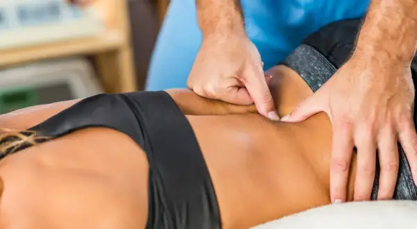 Mains d'un kinésithérapeute massant le dos d'une femme pour soulager un trouble musculo squelettique.