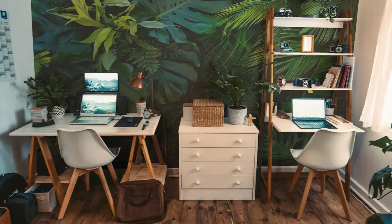 Un bureau chaleureux avec un mur végétal luxuriant, deux postes de travail équipés d'ordinateurs portables, des étagères remplies d'objets décoratifs et de livres, le tout sur un parquet en bois.