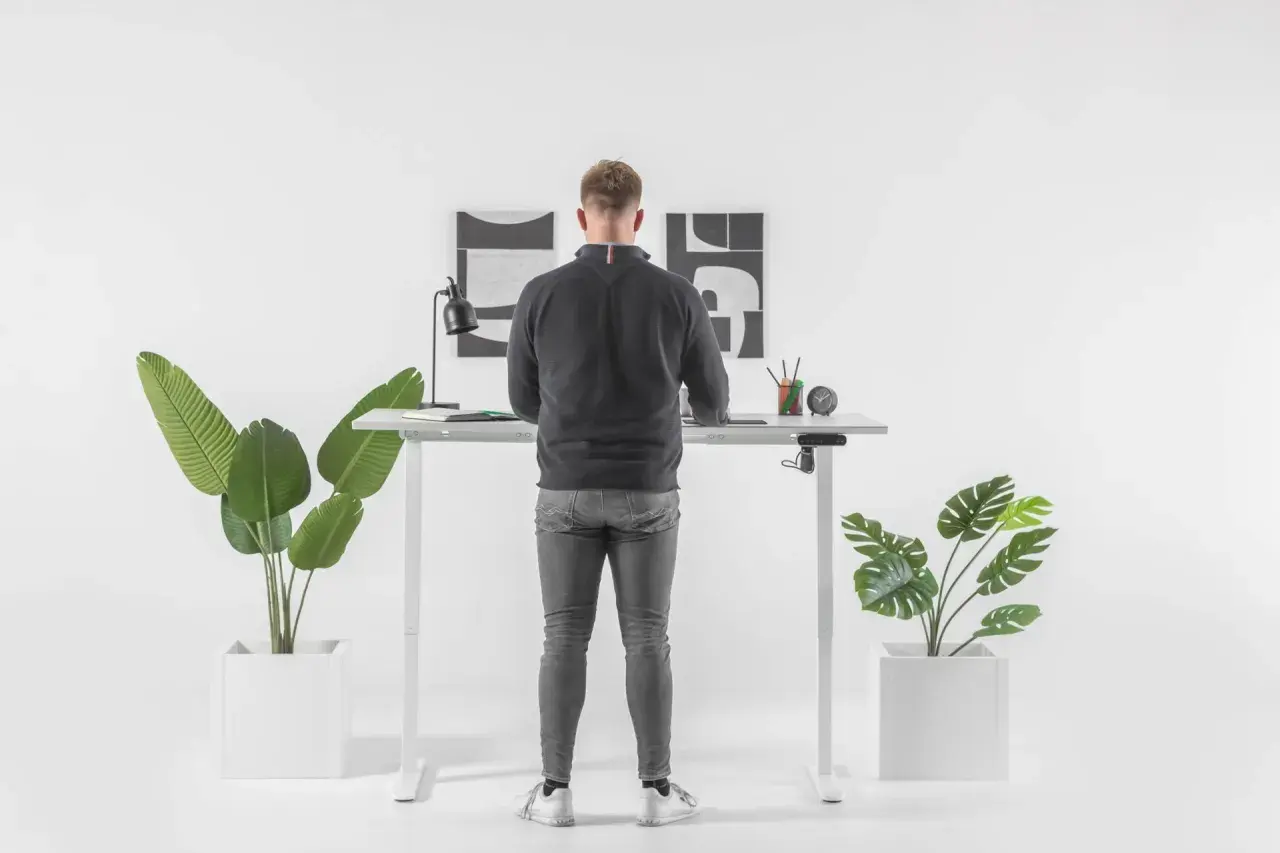 Un homme debout à un bureau réglable en hauteur. Il se demande combien de temps rester debout par jour pour un bien-être optimal.
