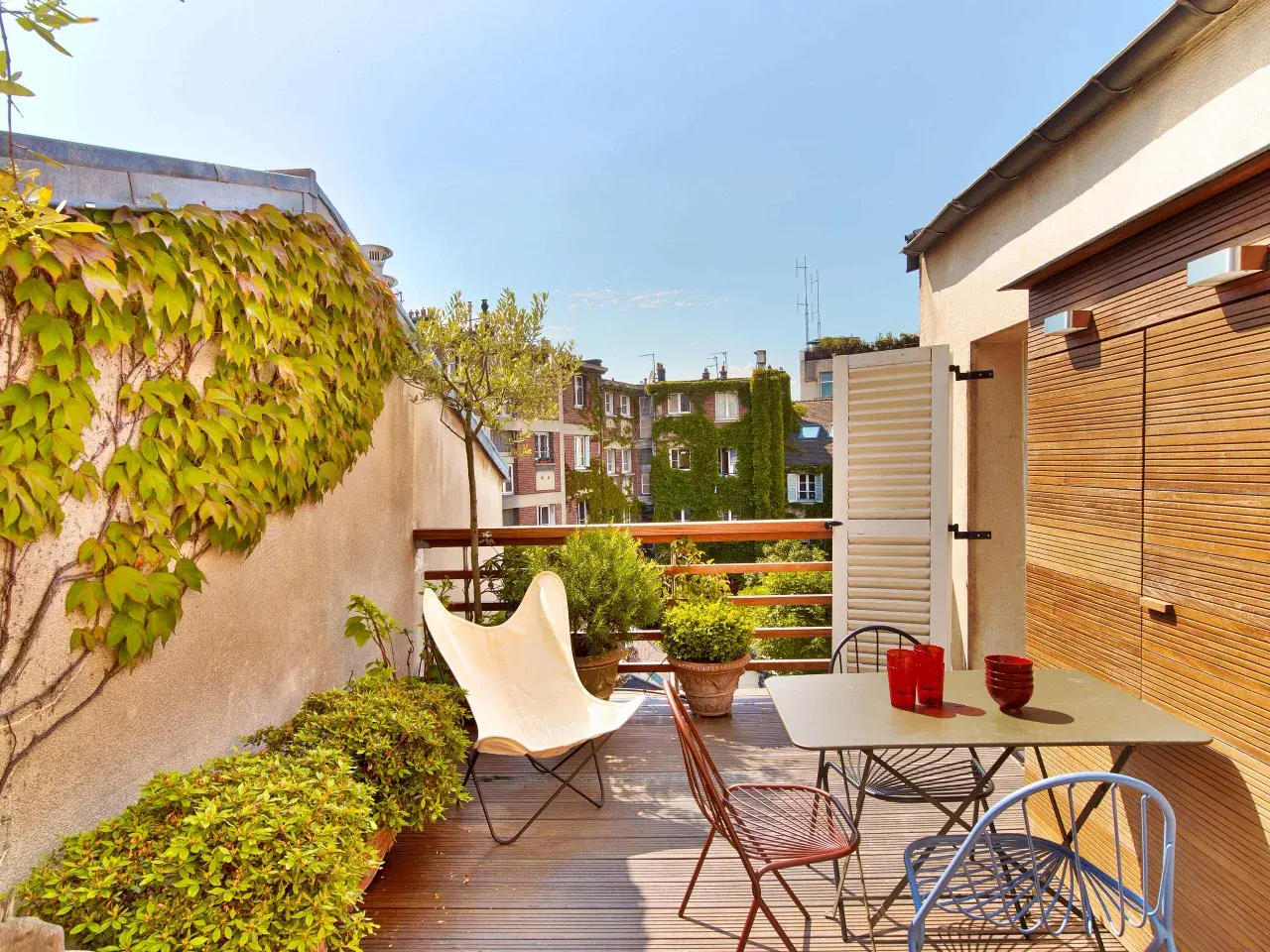 Une belle idee amenagement terrasse : mobilier coloré, plantes luxuriantes et vue sur les toits. Parfait pour un moment de détente.