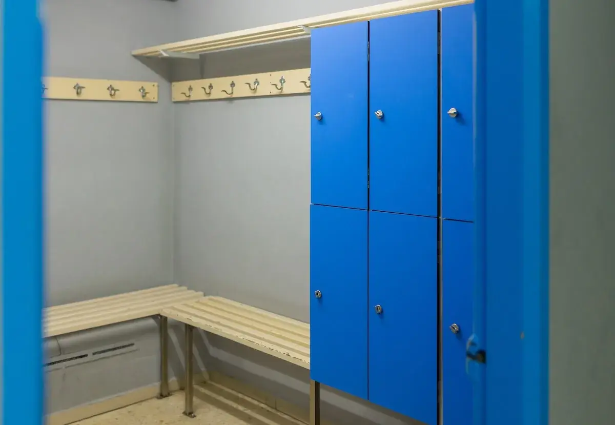 Vestiaire d'entreprise avec casiers personnels bleus, bancs en bois et patères.