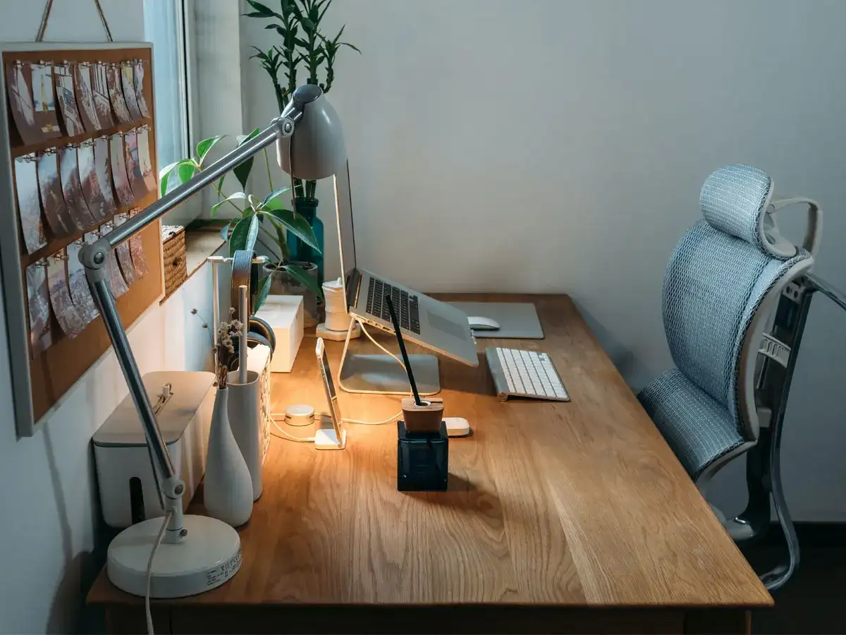 Bureau de **poste en télétravail** bien organisé avec lampe, ordinateur portable, clavier, souris et plante verte. Chaise ergonomique à proximité.