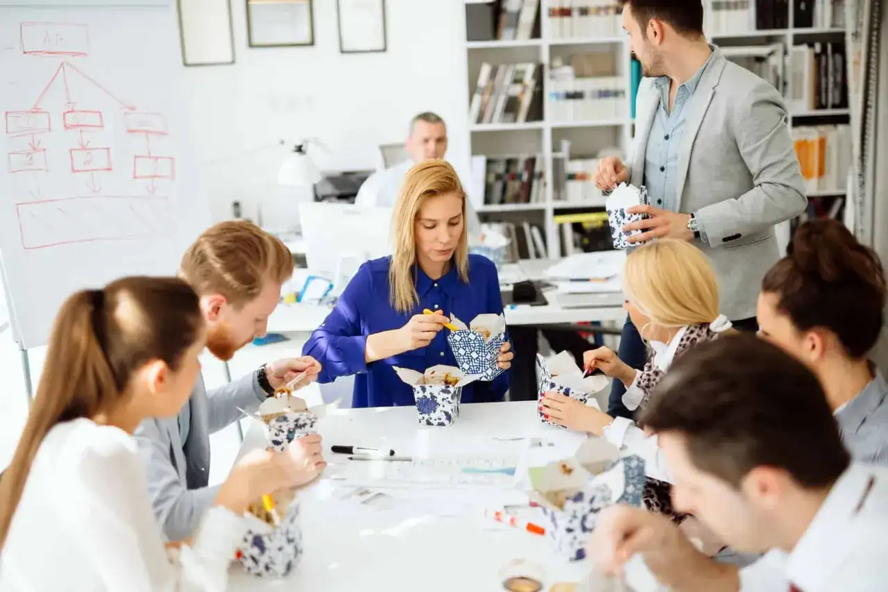 Une équipe profite d'un pause repas, partageant des boîtes de nouilles. Le code du travail permet ces moments de convivialité.