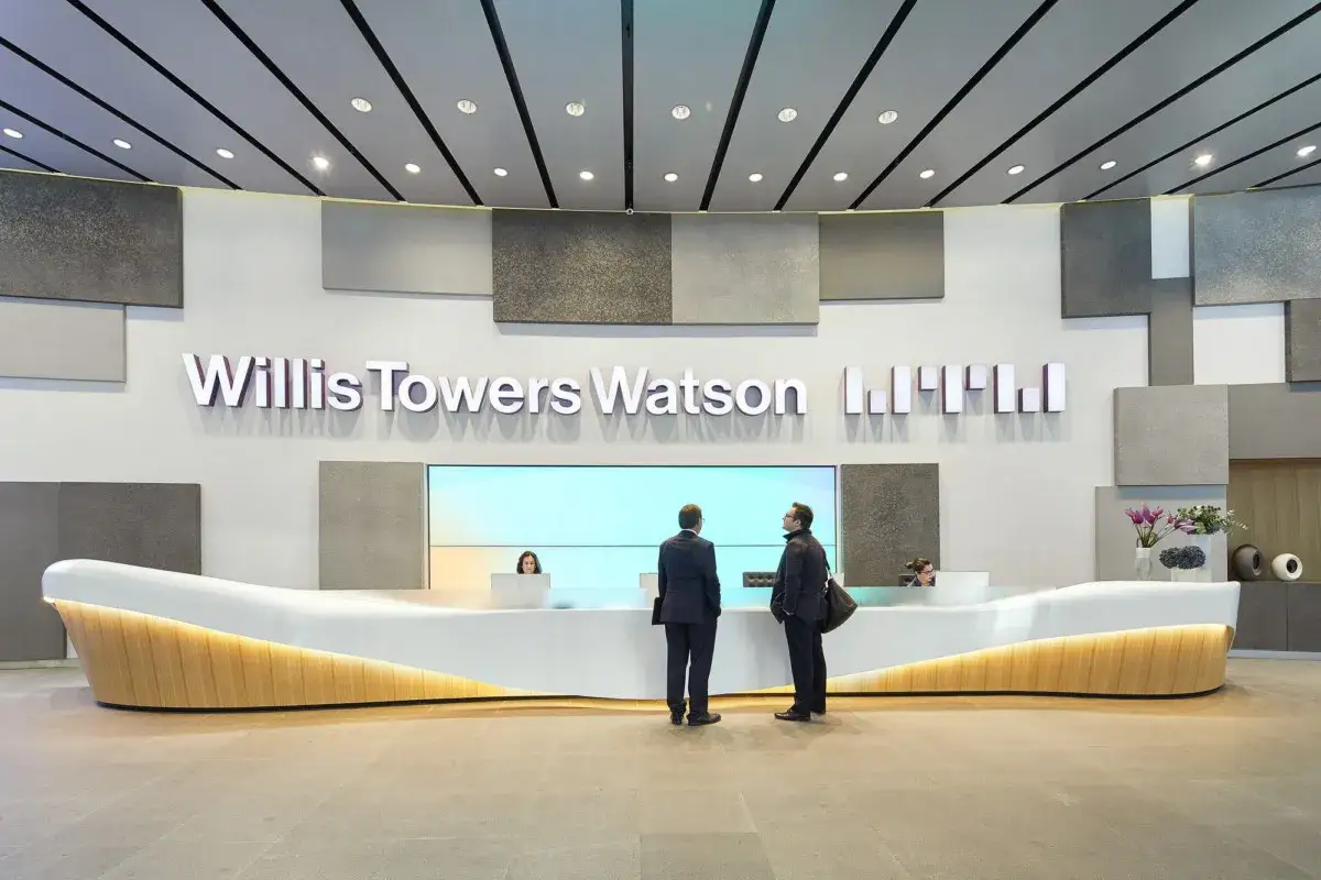 Hall d'entr&eacute;e entreprise Willis Towers Watson. Deux hommes attendent &agrave; la r&eacute;ception moderne, &eacute;clair&eacute;e par des lumi&egrave;res douces.