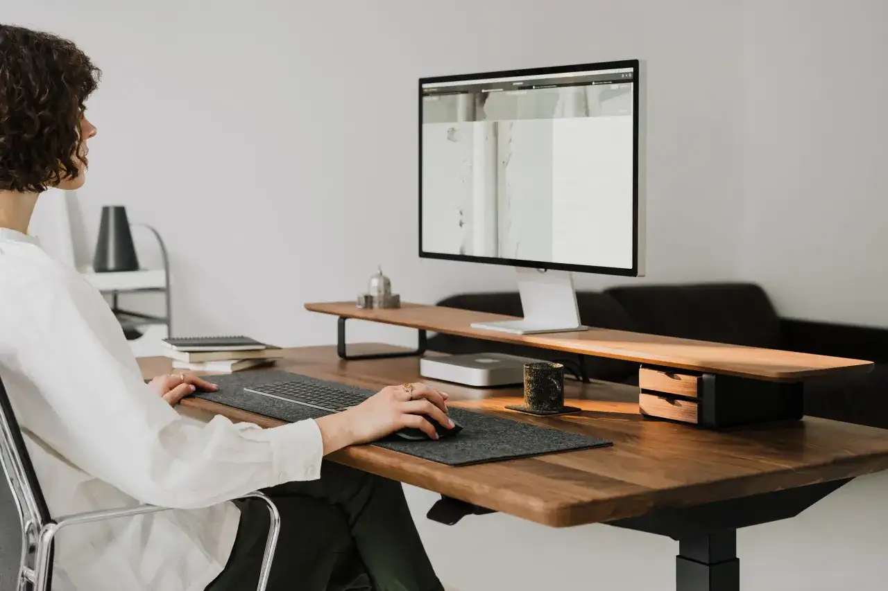 Aménagement bureau atelier : une femme aux cheveux bouclés travaille sur son ordinateur, dans un espace de travail moderne et épuré.