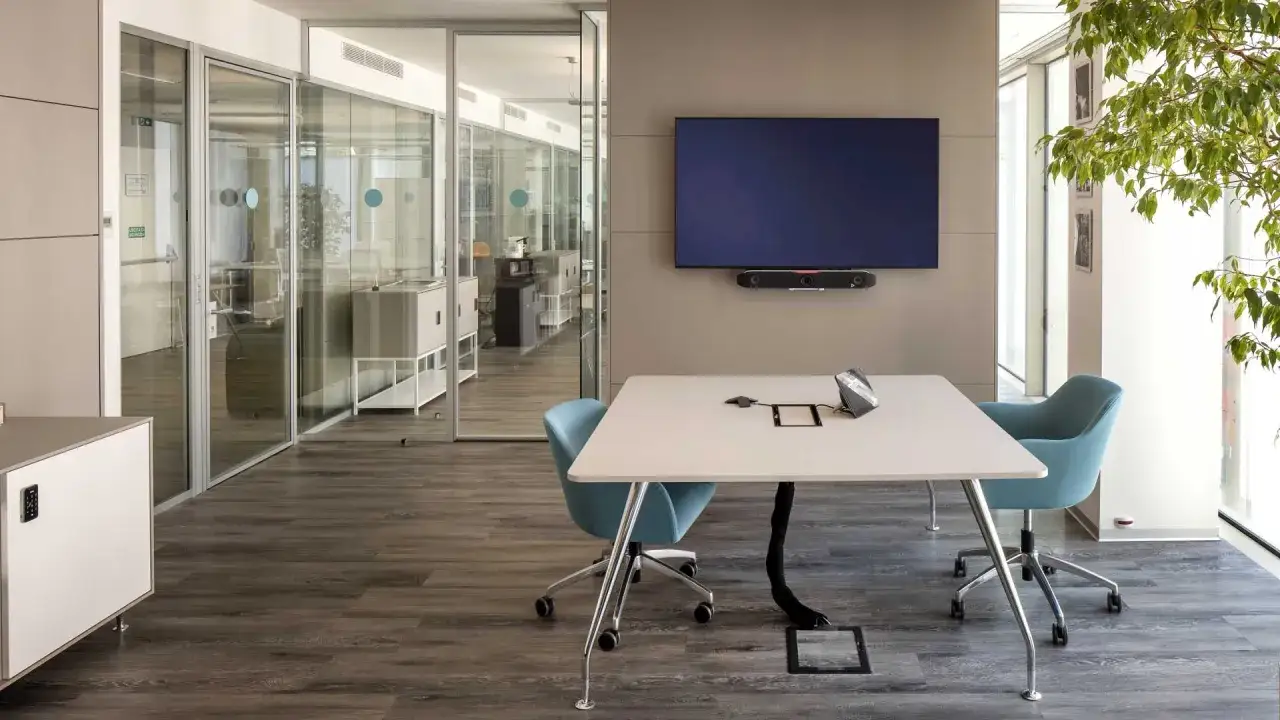 Bureau moderne avec table de conférence, écrans, fauteuils bleus et plantes vertes. Une ambiance qui reflète la tendance déco bureau professionnel.