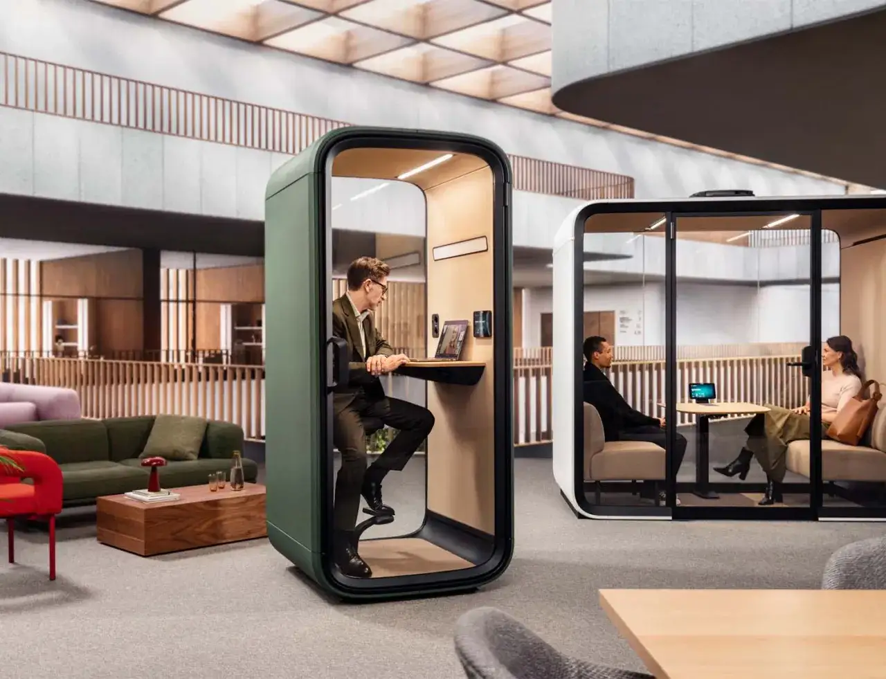 Un homme travaille dans une cabine individuelle, tandis qu'un couple discute dans une autre. Un exemple d'open space design favorisant la concentration et la collaboration.