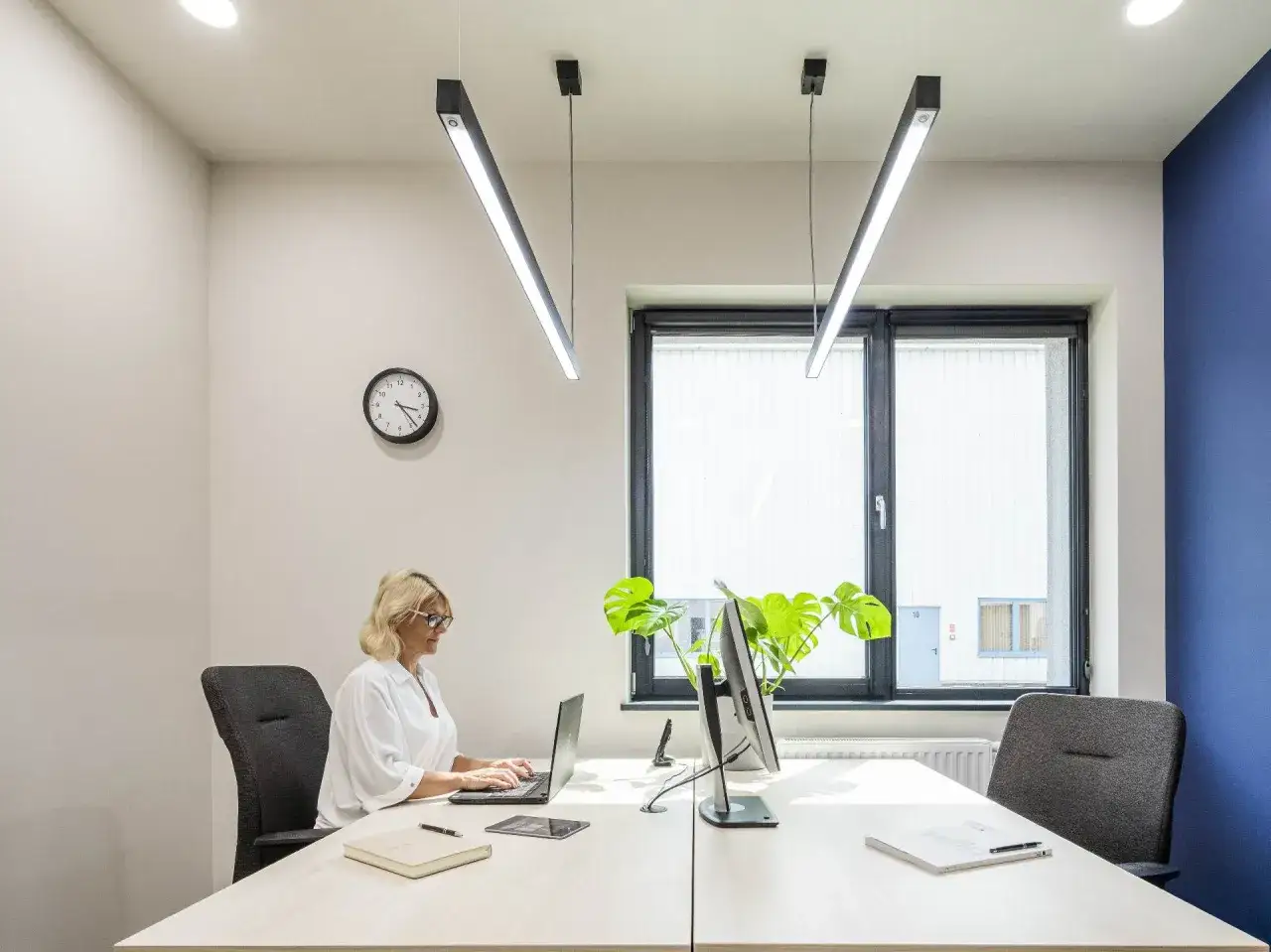 Bureau moderne avec femme travaillant sur ordinateur portable. L'éclairage LED au plafond respecte la norme éclairage lux pour un confort visuel optimal.