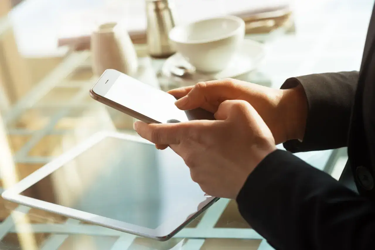 Mains tenant un smartphone, avec une tablette en arri&egrave;re-plan. L'ergonomie mobile est essentielle pour une utilisation confortable.