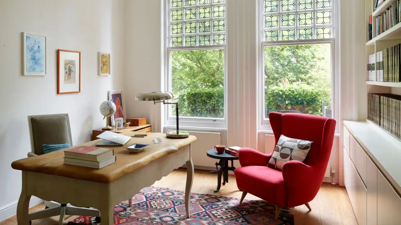 Un bureau chaleureux avec un fauteuil rouge vif, un bureau en bois, des livres et une vue sur la verdure.