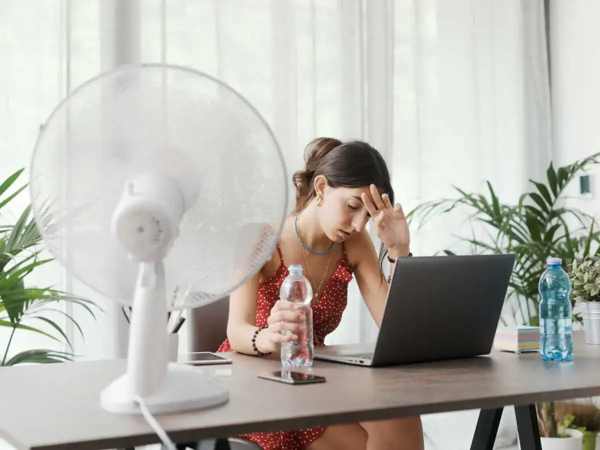 Une femme transpire &agrave; son bureau, ventilateur en marche, pour lutter contre la temp&eacute;rature maximale. Elle tient une bouteille d'eau.