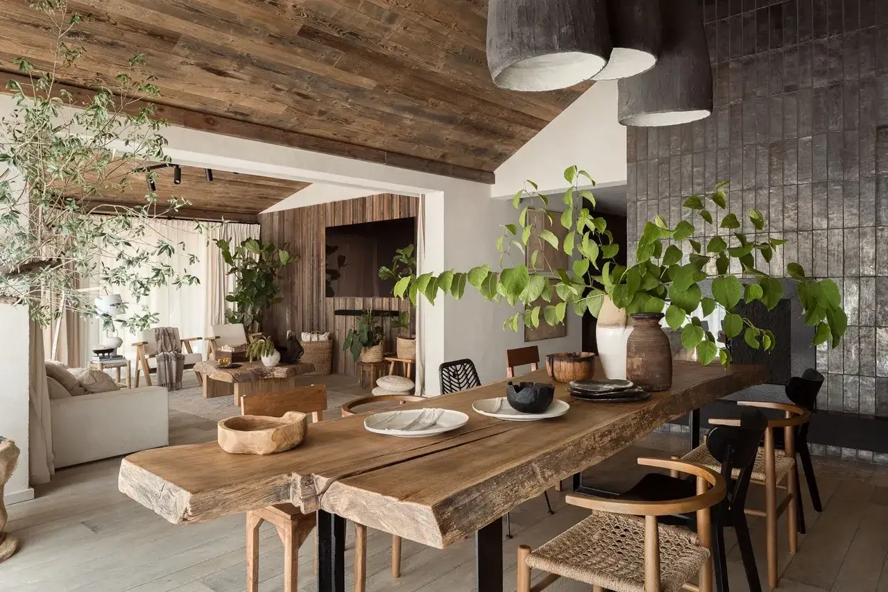 Un salon et une salle &agrave; manger chaleureux, avec des mat&eacute;riaux naturels, des plantes et une grande table en bois brut. La biophilie est &eacute;vidente dans cet espace invitant.