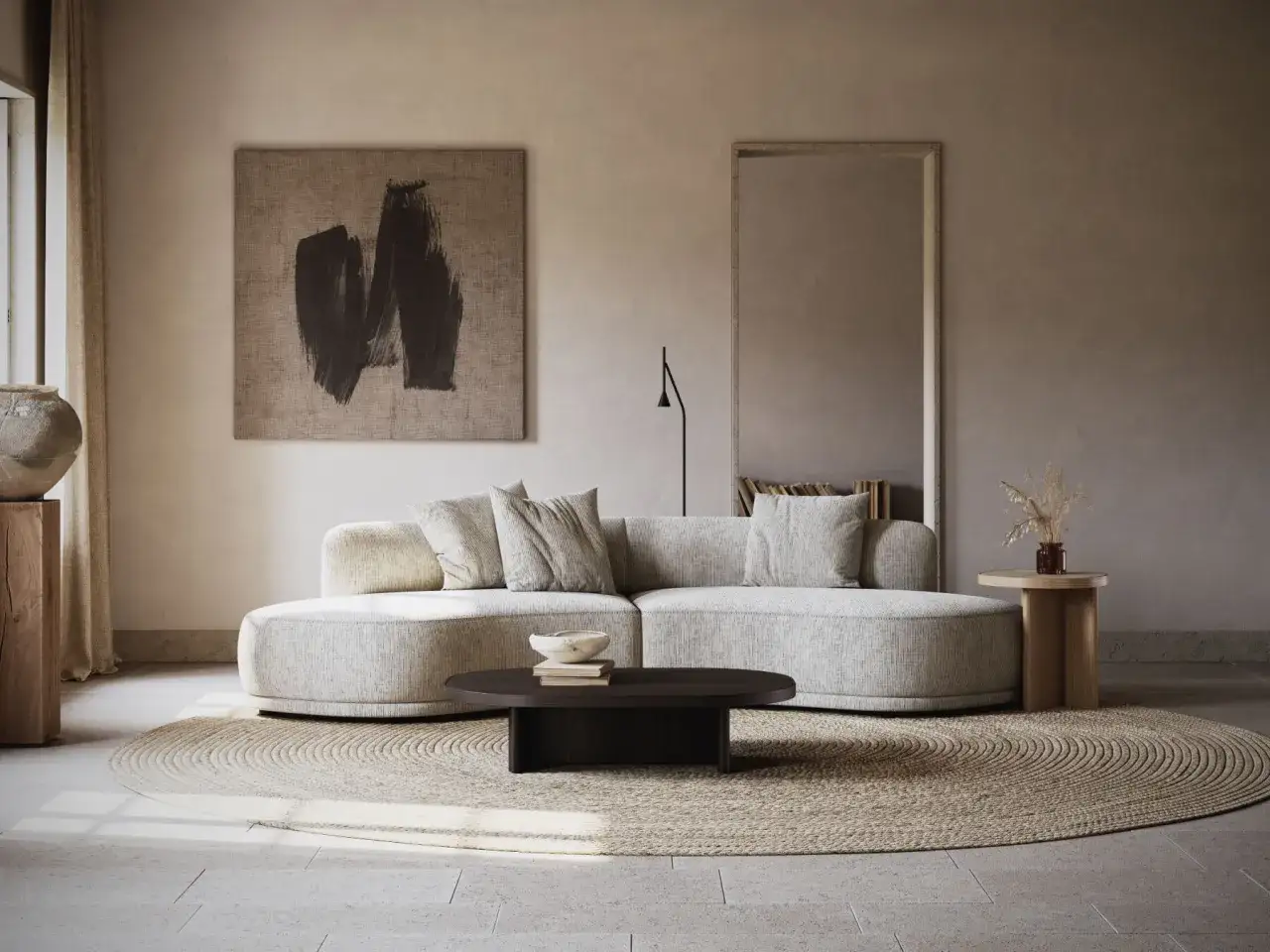Salon cosy aux couleurs neutres chaudes. Canap&eacute; arrondi, tapis rond en jonc de mer, table basse sombre et art abstrait.