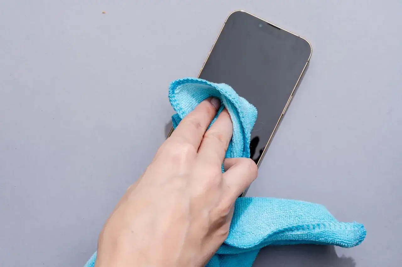 Main d'une personne utilisant un chiffon bleu pour nettoyer l'&eacute;cran d'un t&eacute;l&eacute;phone.