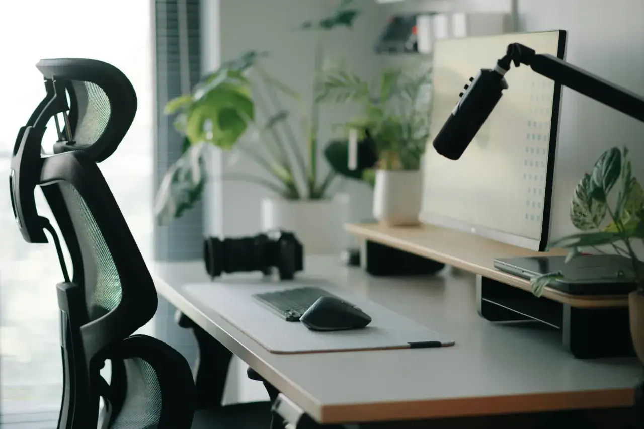 Un bureau moderne pr&ecirc;t pour le travail, avec une chaise ergonomique, un &eacute;cran, un microphone, un appareil photo et des plantes vertes pour un environnement de travail agr&eacute;able.