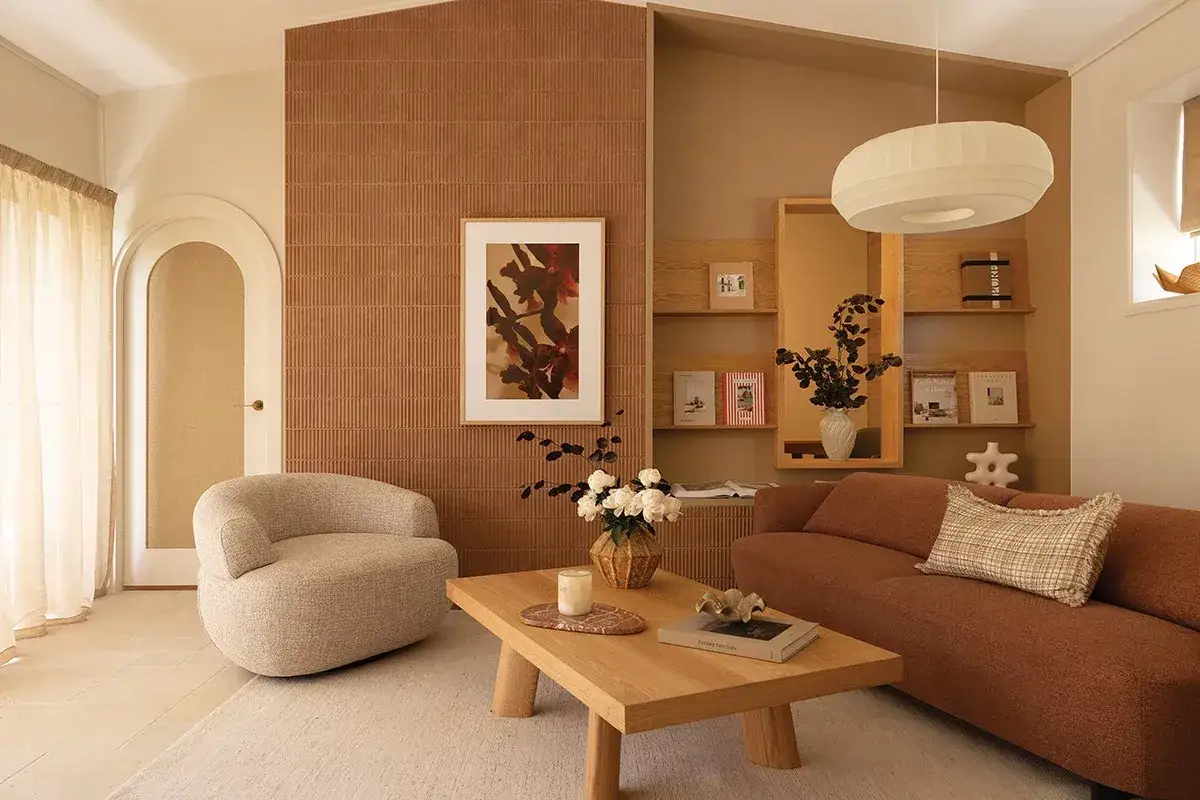 Salon chaleureux avec canap&eacute; rouille, fauteuil bouclette et table basse en bois. Le mur textur&eacute; ocre &eacute;voque la couleur de la cr&eacute;ativit&eacute;.