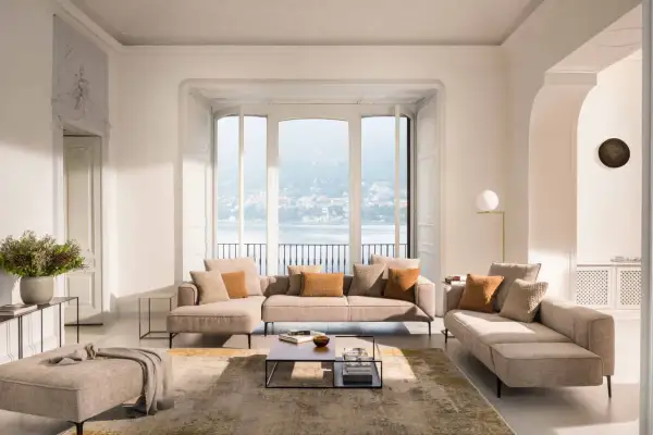 Salon lumineux avec canapé modulable, pouf et table basse, dans un style design scandinave épuré. Vue sur un lac.