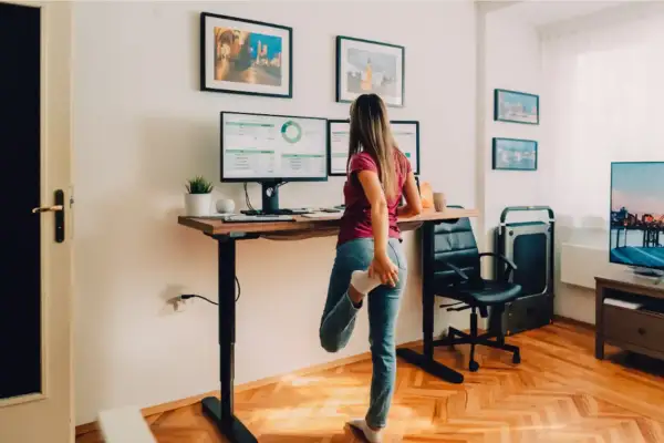 Femme s'étirant à son bureau réglable en hauteur, profitant du confort au bureau avec ses deux écrans.