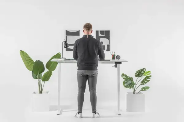 Un homme debout à un bureau réglable en hauteur. Il se demande combien de temps rester debout par jour pour un bien-être optimal.