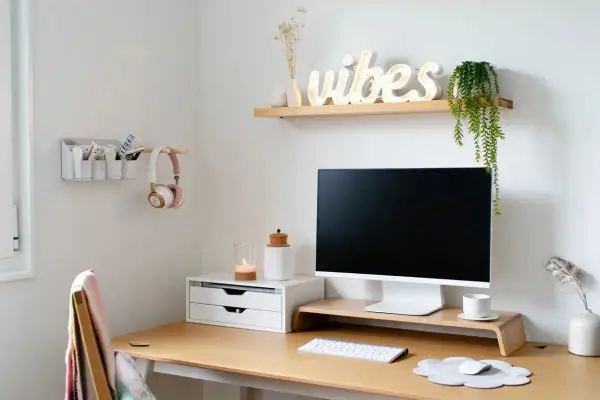 Un coin bureau fonctionnel pour un petit espace. Un bureau en bois avec un écran, un clavier, une souris, des écouteurs roses et une décoration murale "vibes".