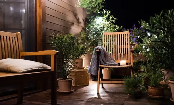 Ambiance chaleureuse sur une petite terrasse : deux chaises en bois, coussin, plaid, bougie et plantes vertes illuminées par des guirlandes.