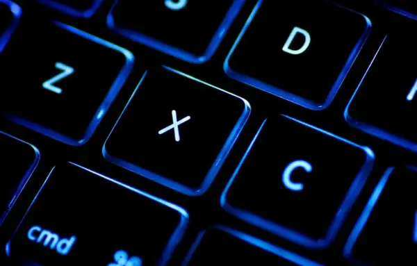 Gros plan sur un clavier rétroéclairé, les touches noires illuminées de bleu. On distingue les lettres Z, X, C, D et la touche "cmd". Un clavier BÉPO pour une frappe optimisée.
