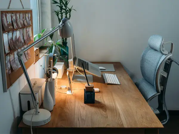 Bureau de **poste en télétravail** bien organisé avec lampe, ordinateur portable, clavier, souris et plante verte. Chaise ergonomique à proximité.