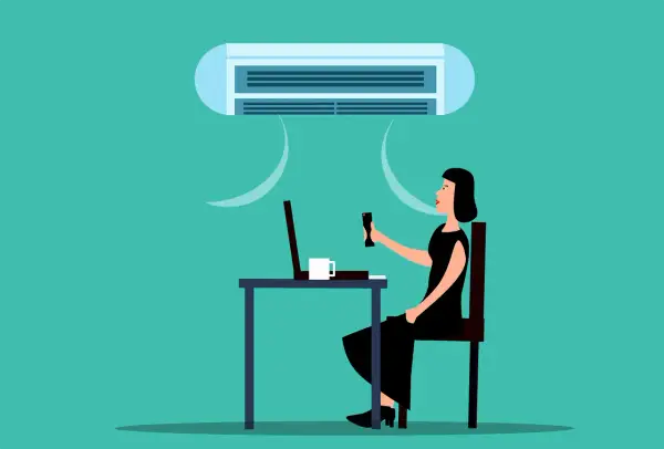 Une femme ajuste la climatisation de son bureau, cherchant la température idéale pour respecter le code du travail.