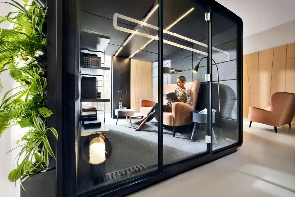 Une femme lit dans un bureau ouvert, un espace flex moderne avec une paroi végétale luxuriante et des cabines privées.