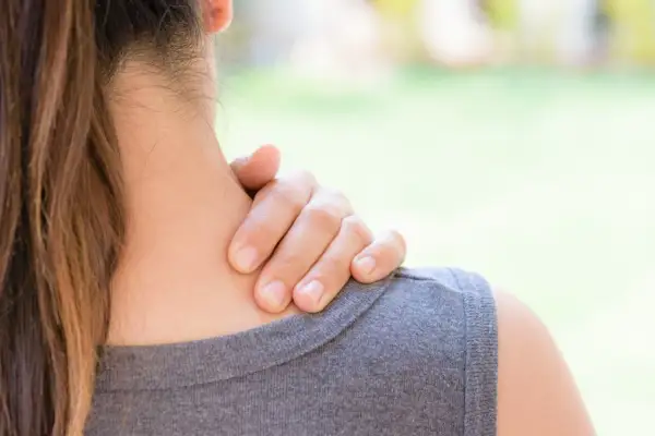 Une main masse la nuque d'une femme, suggérant un besoin d'échauffement cervicales après une longue journée.