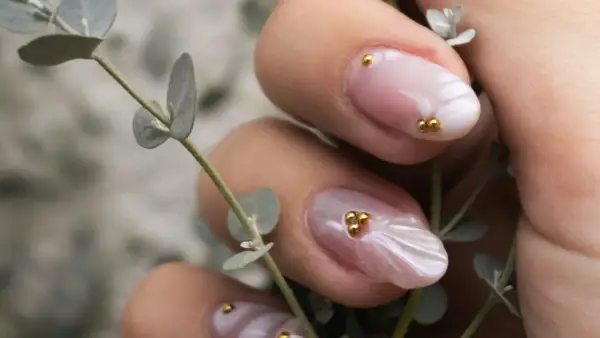 Manucure délicate aux perles dorées sur fond rose quartz, évoquant la douceur d'une fleur.