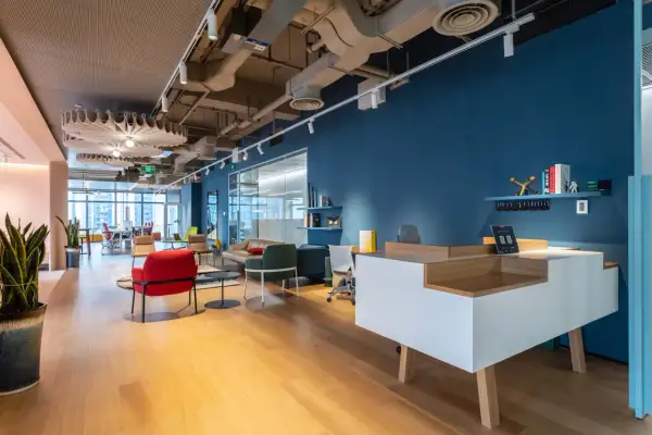 Un hall d'entrée d'entreprise moderne avec un bureau d'accueil blanc et bois, des fauteuils colorés et une grande fenêtre.
