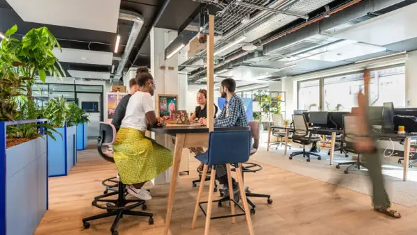 Aménagement bureau atelier : des collaborateurs échangent autour d'une table haute, dans un espace lumineux et végétalisé.
