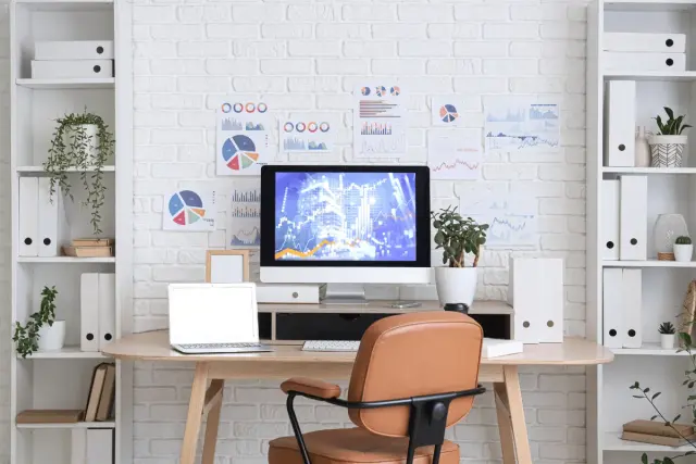 Bureau moderne avec écran d'ordinateur affichant des graphiques, un ordinateur portable et une chaise confortable pour une ergonomie au travail optimale.